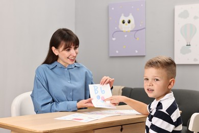 Photo of Smiling speech therapist working with little boy at table in autism treatment center