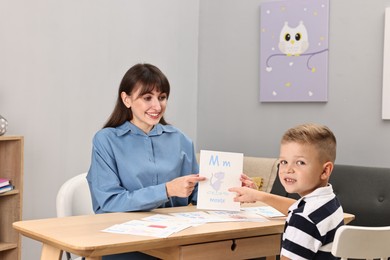 Photo of Smiling speech therapist working with little boy at table in autism treatment center