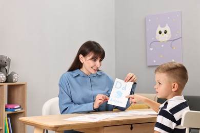 Photo of Smiling speech therapist working with little boy at table in autism treatment center