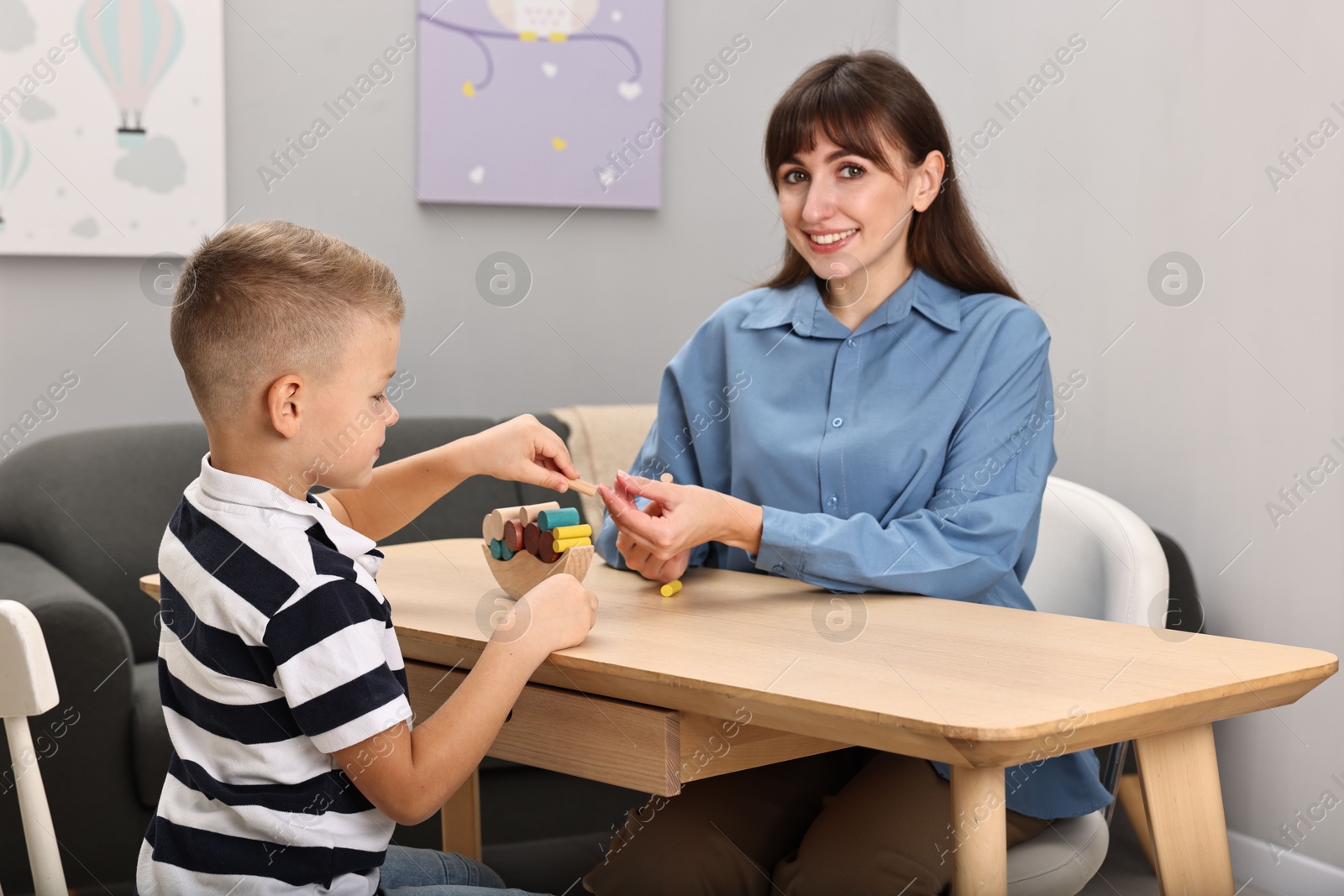 Photo of Autism therapy. Smiling psychologist and little boy playing with educational toy at table in mental health center