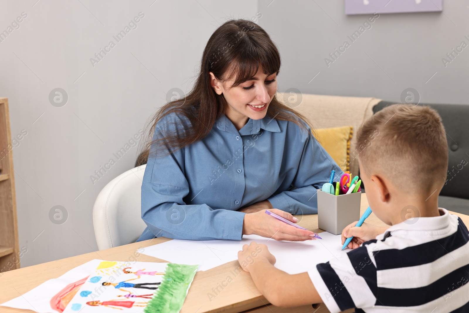 Photo of Autism therapy. Smiling psychologist and little boy drawing pictures at table in mental health center