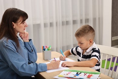 Photo of Autism therapy. Psychologist and little boy drawing pictures at table in mental health center