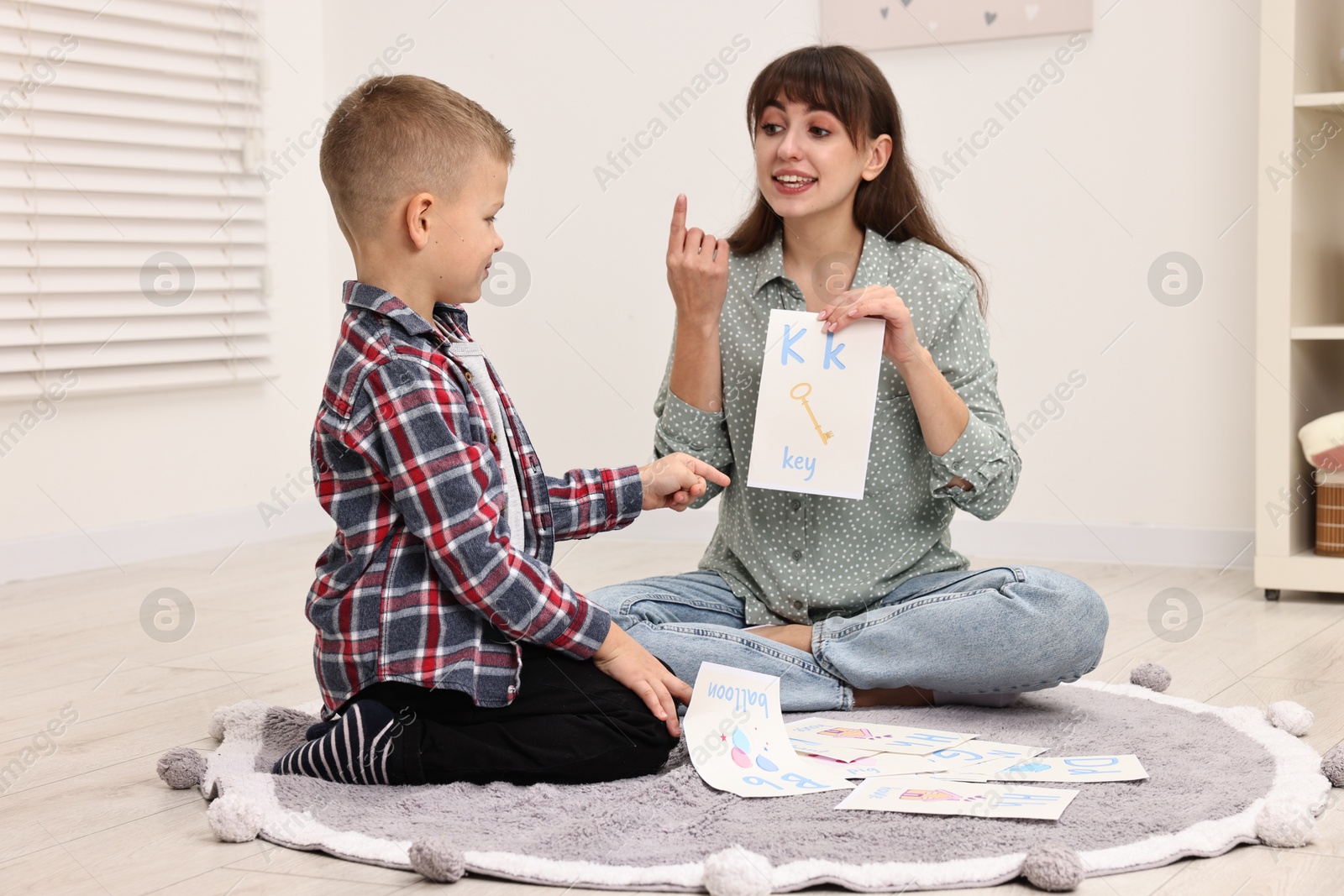 Photo of Smiling speech therapist working with little boy on floor in autism treatment center