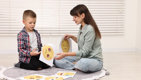 Autism therapy. Little boy choosing emoticon with psychologist in mental health center