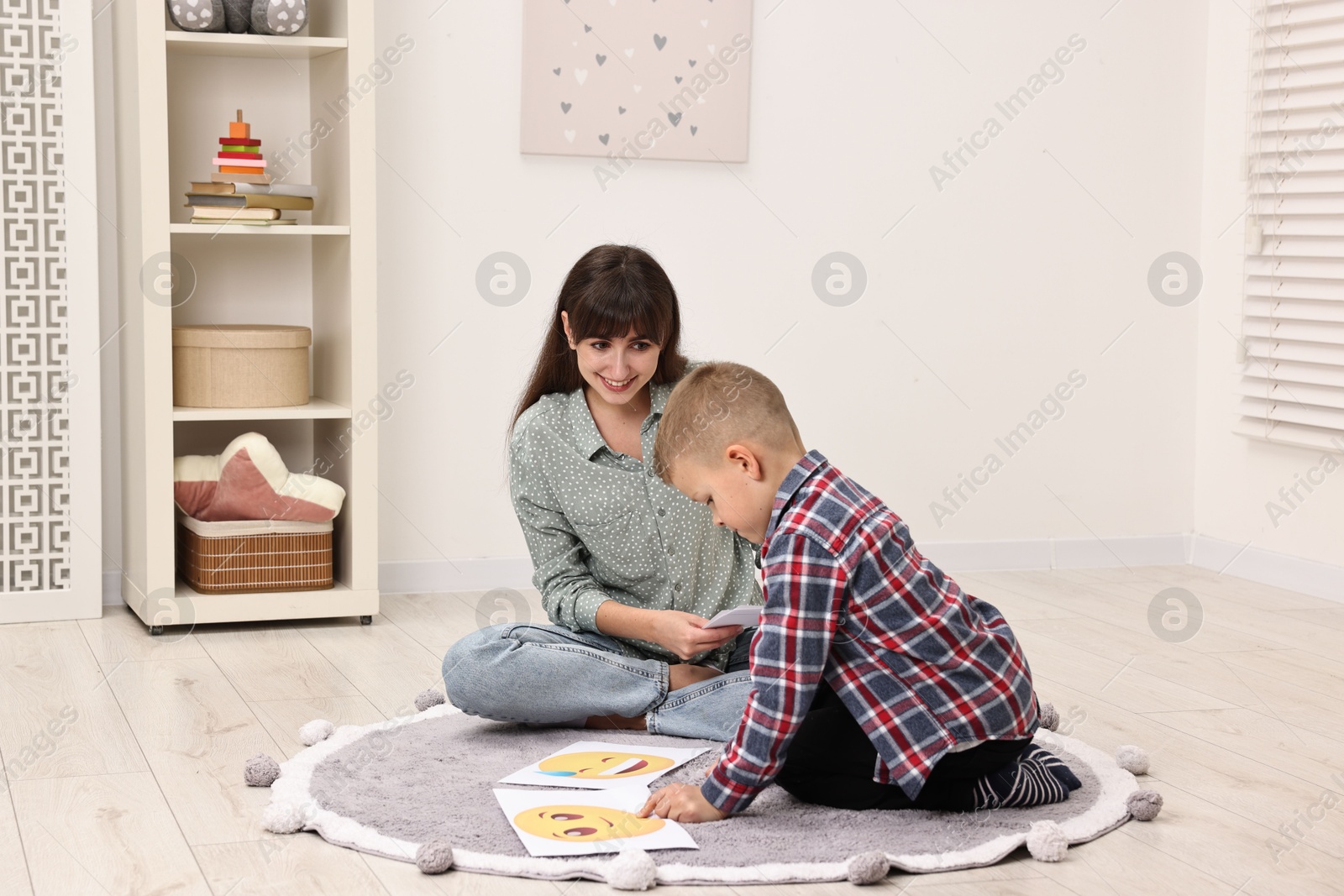 Photo of Autism therapy. Little boy choosing emoticon with smiling psychologist in mental health center