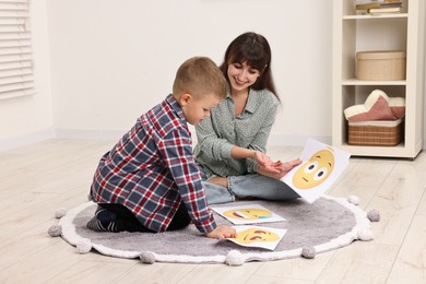 Autism therapy. Little boy choosing emoticon with smiling psychologist in mental health center