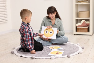 Photo of Autism therapy. Little boy choosing emoticon with smiling psychologist in mental health center