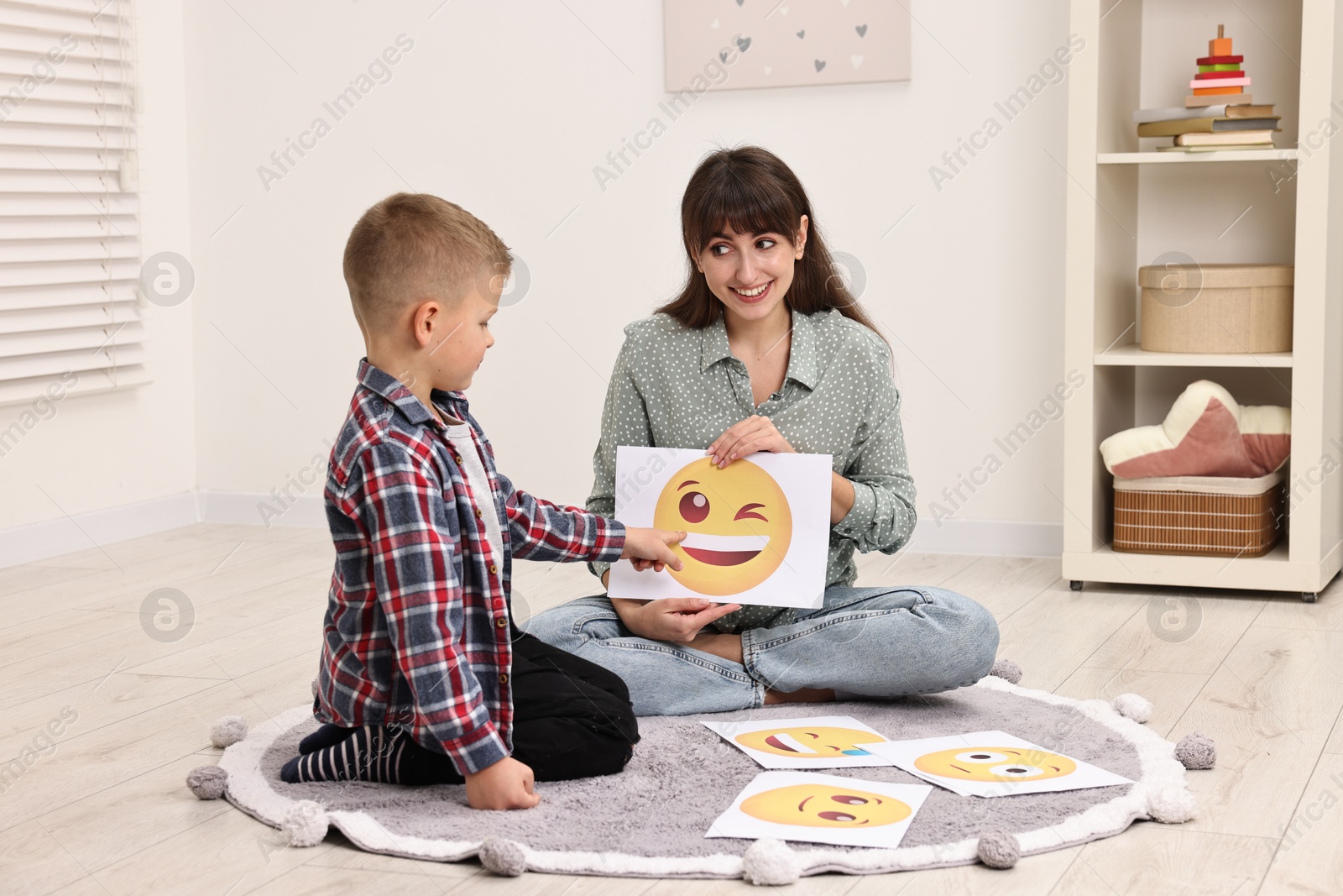 Photo of Autism therapy. Little boy choosing emoticon with smiling psychologist in mental health center