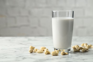 Photo of Fresh cashew milk in glass and nuts on white marble table. Space for text