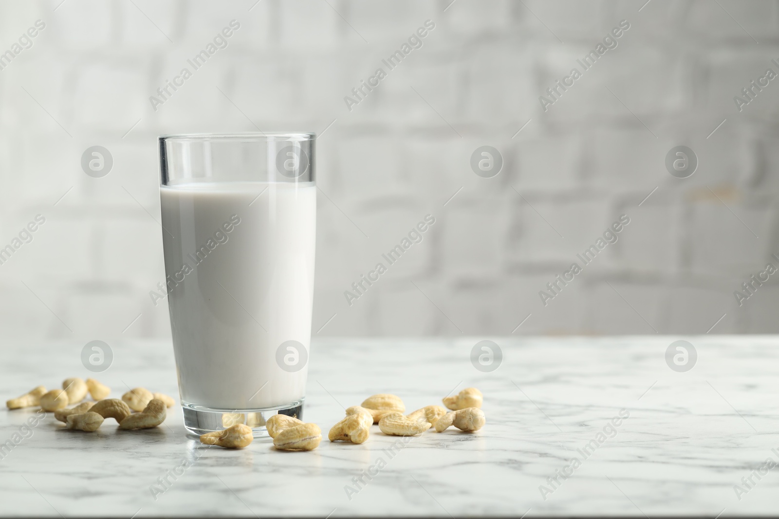 Photo of Fresh cashew milk in glass and nuts on white marble table. Space for text