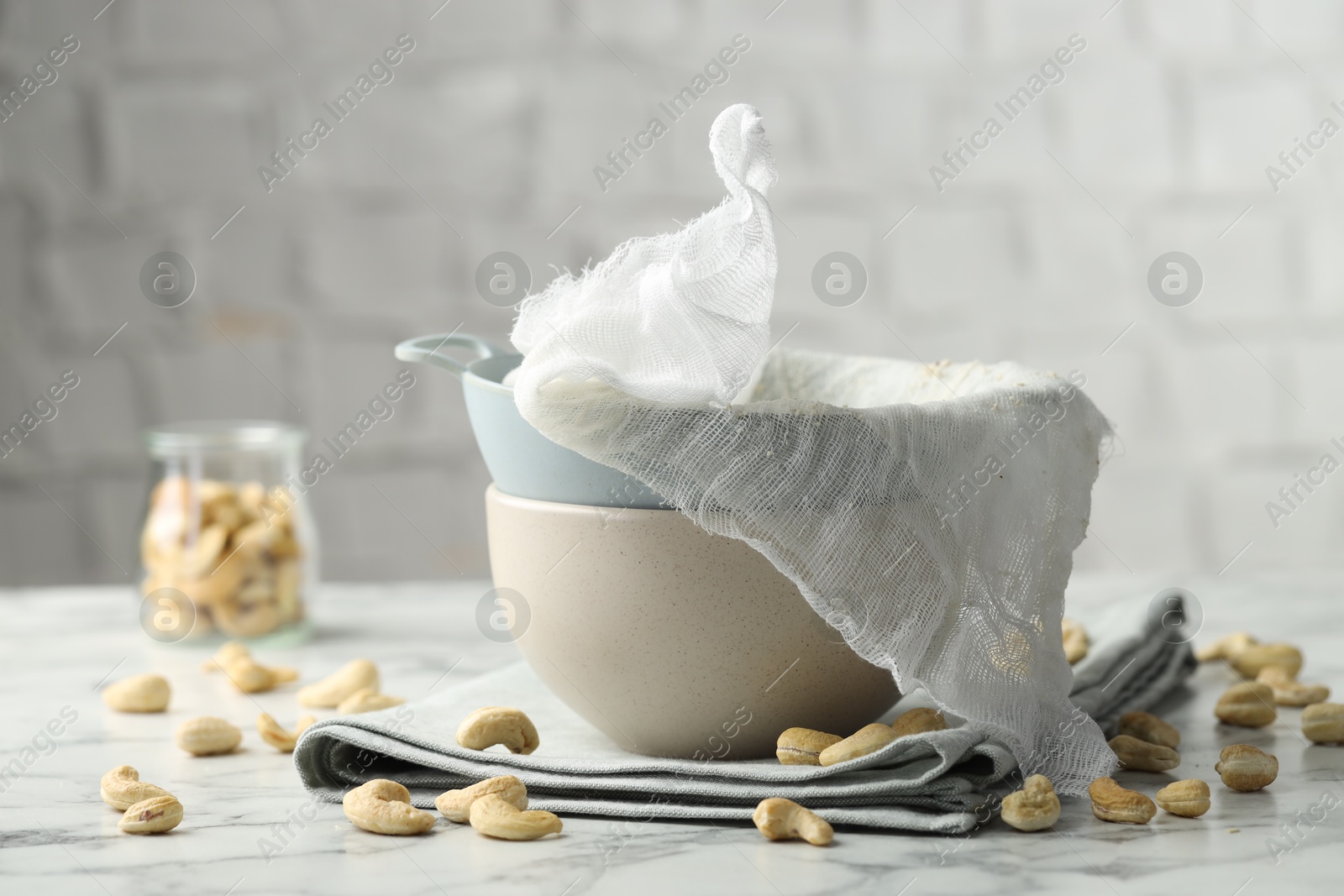 Photo of Making cashew milk. Colander, cheesecloth, bowl and nuts on white marble table indoors, closeup