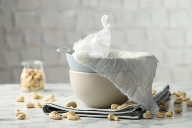 Making cashew milk. Colander, cheesecloth, bowl and nuts on white marble table indoors, closeup