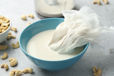 Making cashew milk. Cheesecloth and milk in bowl among nuts on grey table indoors, closeup