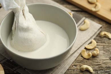 Making cashew milk. Cheesecloth and milk in bowl among nuts on wooden table, closeup