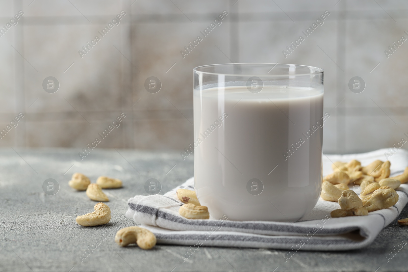 Photo of Fresh cashew milk in glass and nuts on grey textured table, closeup. Space for text