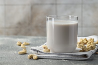 Photo of Fresh cashew milk in glass and nuts on grey textured table, closeup. Space for text