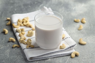 Fresh cashew milk in glass and nuts on grey textured table, closeup