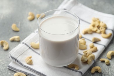 Fresh cashew milk in glass and nuts on grey table, closeup