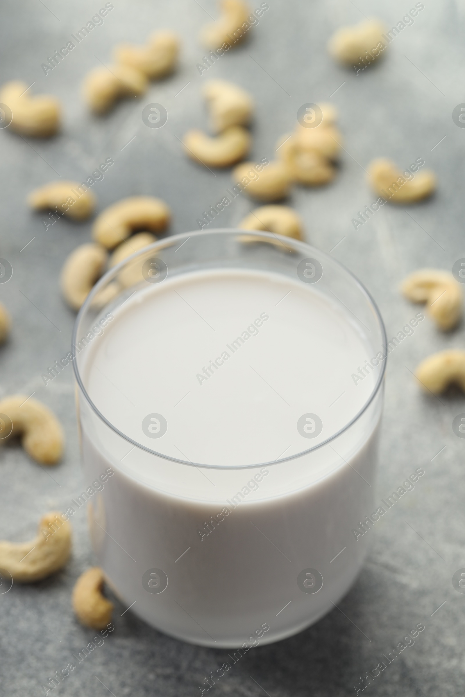 Photo of Fresh cashew milk in glass and nuts on grey table, closeup