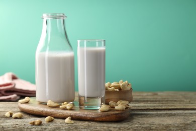 Photo of Fresh cashew milk in glass, bottle and nuts on wooden table against green background, closeup. Space for text