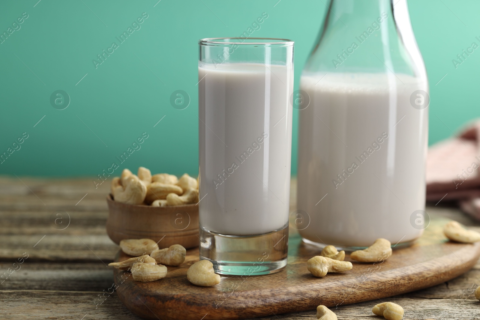 Photo of Fresh cashew milk in glass, bottle and nuts on wooden table against green background, closeup