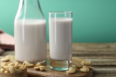 Photo of Fresh cashew milk in glass, bottle and nuts on wooden table against green background, closeup