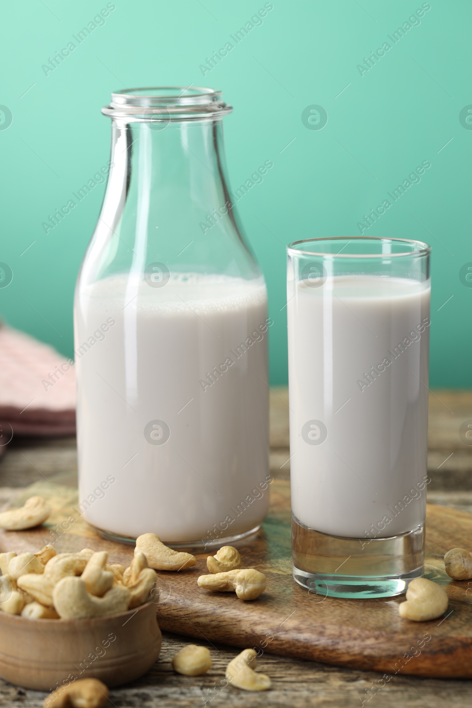 Photo of Fresh cashew milk in glass, bottle and nuts on wooden table against green background, closeup