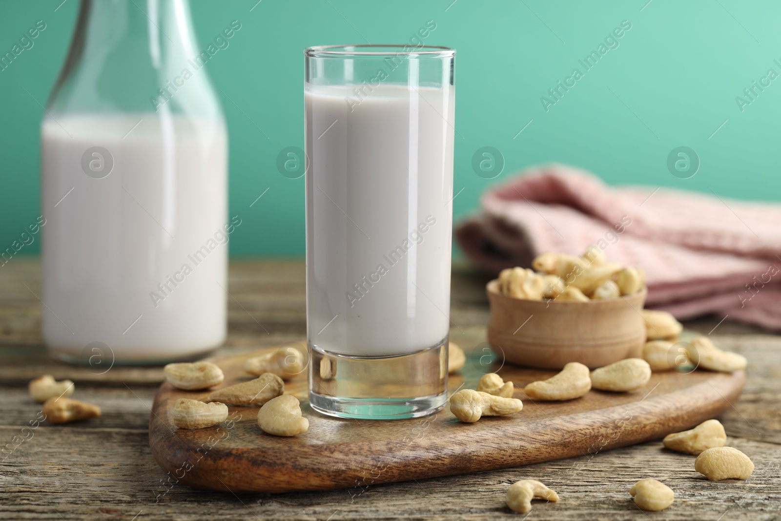 Photo of Fresh cashew milk in glass, bottle and nuts on wooden table against green background, closeup