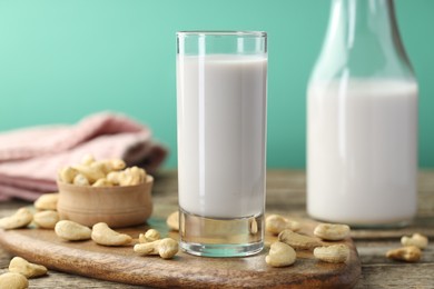 Photo of Fresh cashew milk in glass, bottle and nuts on wooden table against green background, closeup