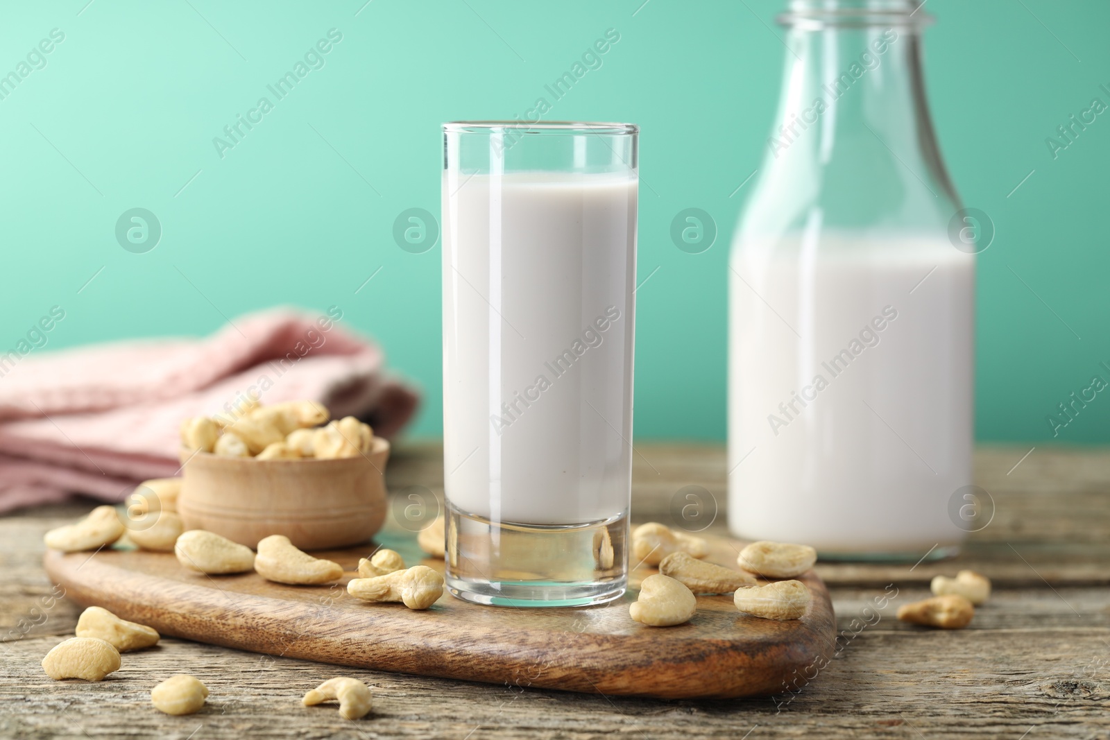 Photo of Fresh cashew milk in glass, bottle and nuts on wooden table against green background, closeup