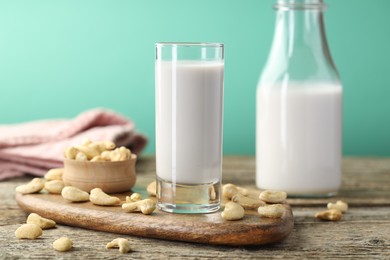 Fresh cashew milk in glass, bottle and nuts on wooden table against green background, closeup