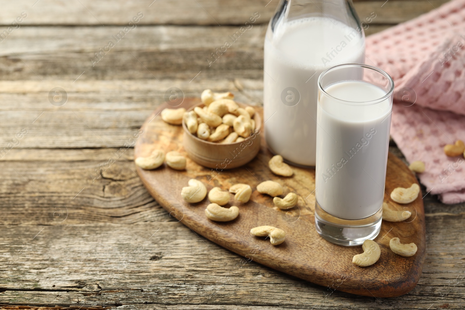 Photo of Fresh cashew milk in glass, bottle and nuts on wooden table, closeup. Space for text