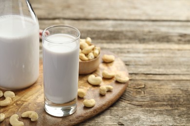 Photo of Fresh cashew milk in glass, bottle and nuts on wooden table, closeup. Space for text