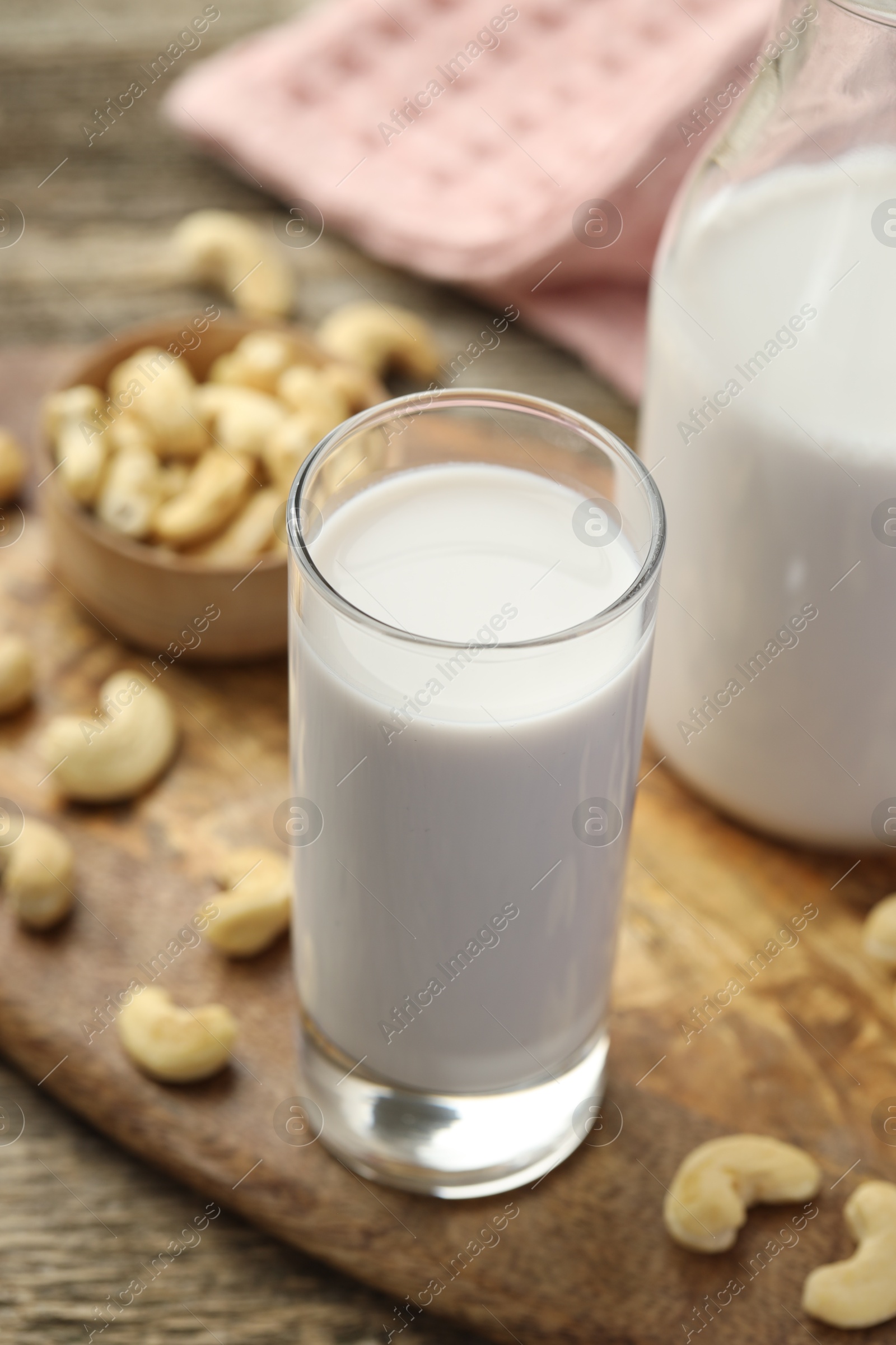 Photo of Fresh cashew milk in glass and nuts on wooden table, closeup