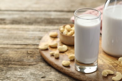 Photo of Fresh cashew milk in glass and nuts on wooden table, closeup. Space for text