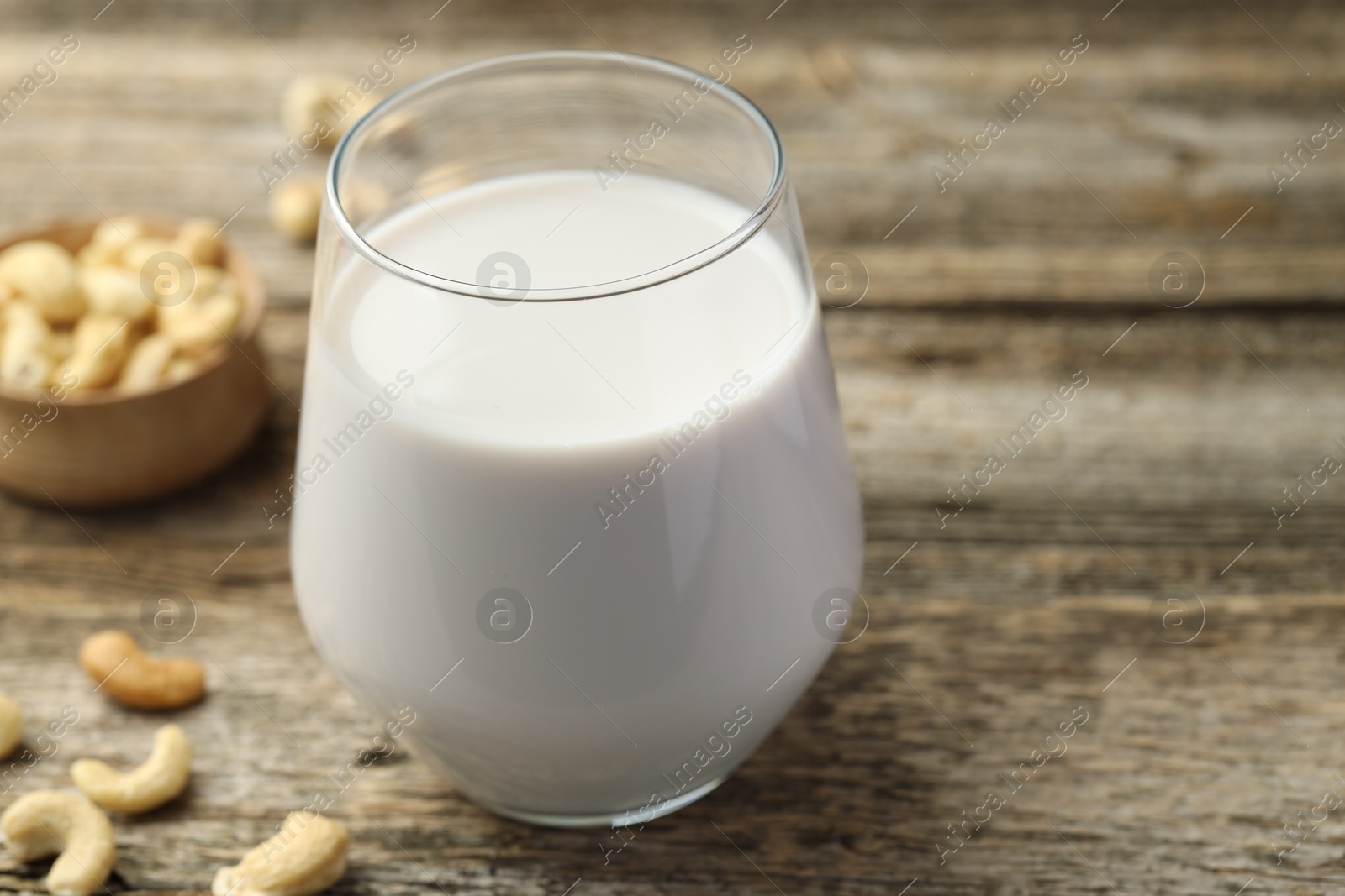 Photo of Fresh cashew milk in glass and nuts on wooden table, closeup