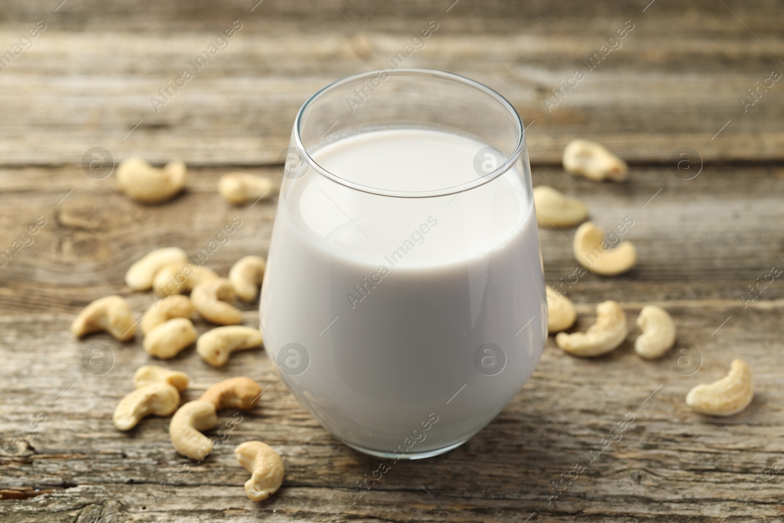 Photo of Fresh cashew milk in glass and nuts on wooden table, closeup