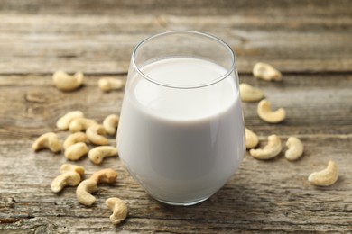 Photo of Fresh cashew milk in glass and nuts on wooden table, closeup