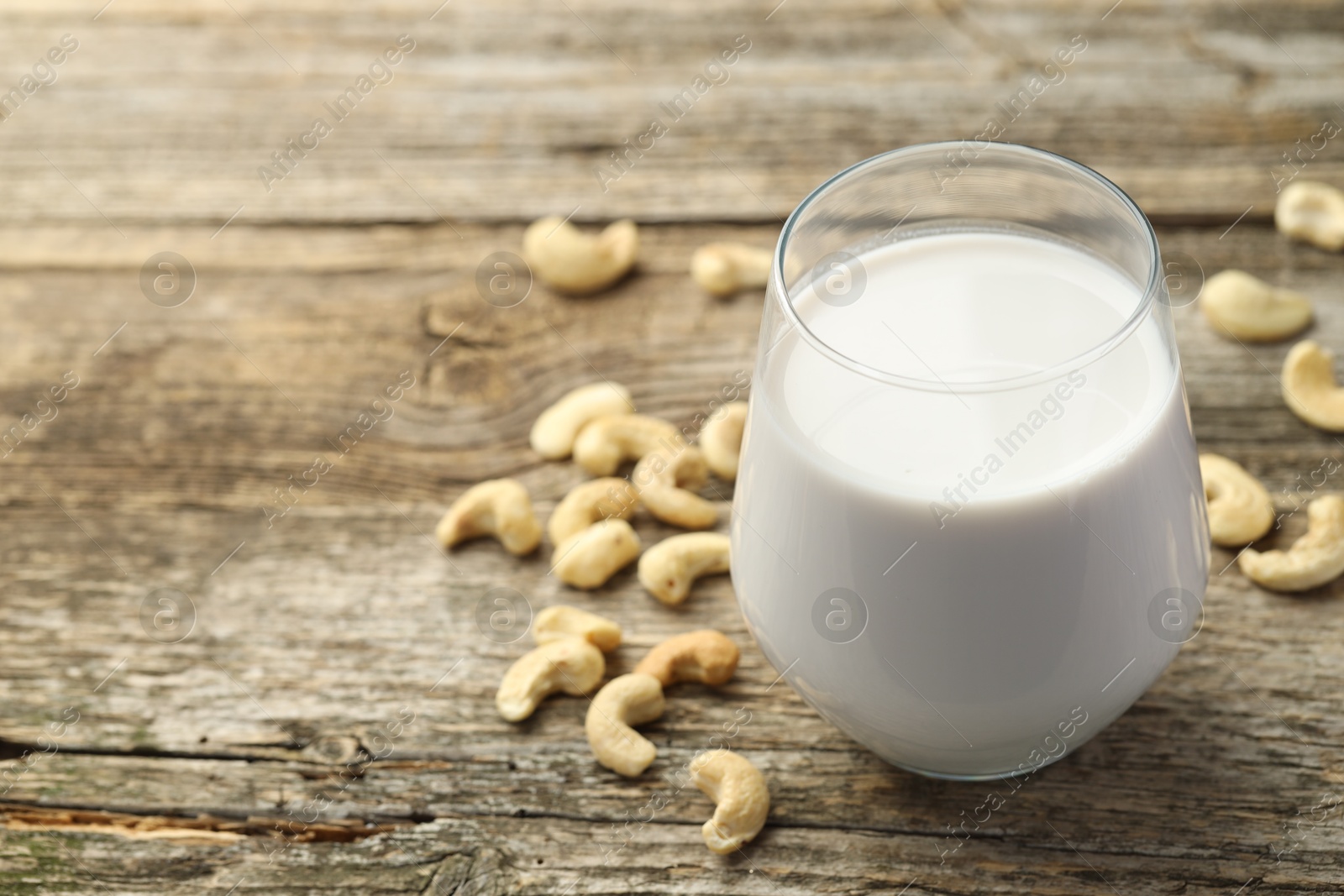 Photo of Fresh cashew milk in glass and nuts on wooden table, closeup. Space for text