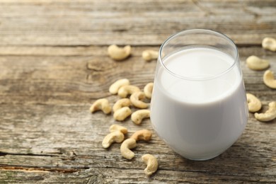 Fresh cashew milk in glass and nuts on wooden table, closeup. Space for text