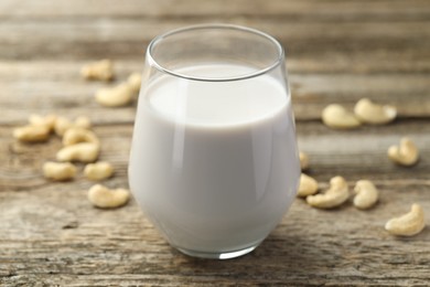 Fresh cashew milk in glass and nuts on wooden table, closeup