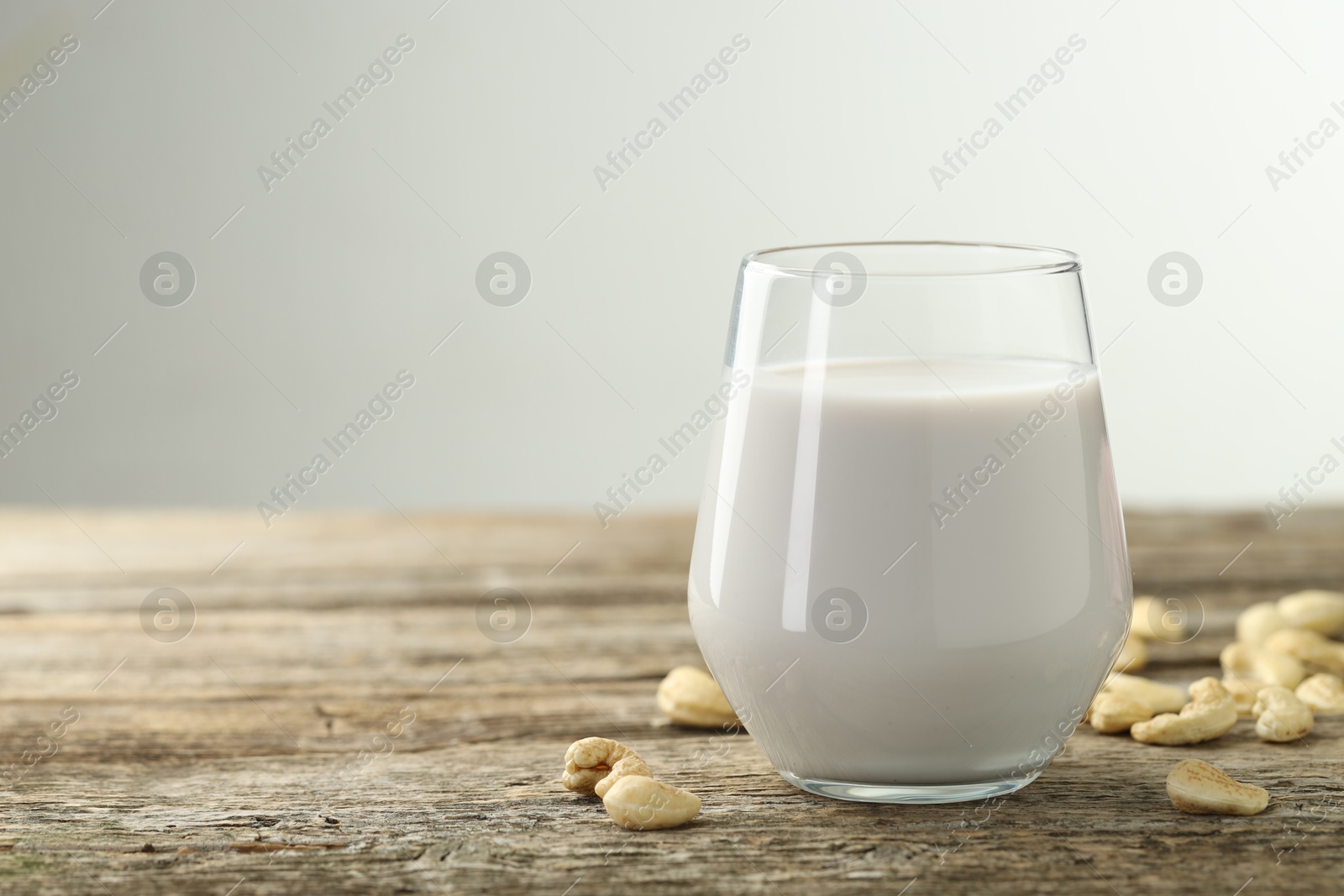 Photo of Fresh cashew milk in glass and nuts on wooden table against light background, closeup. Space for text