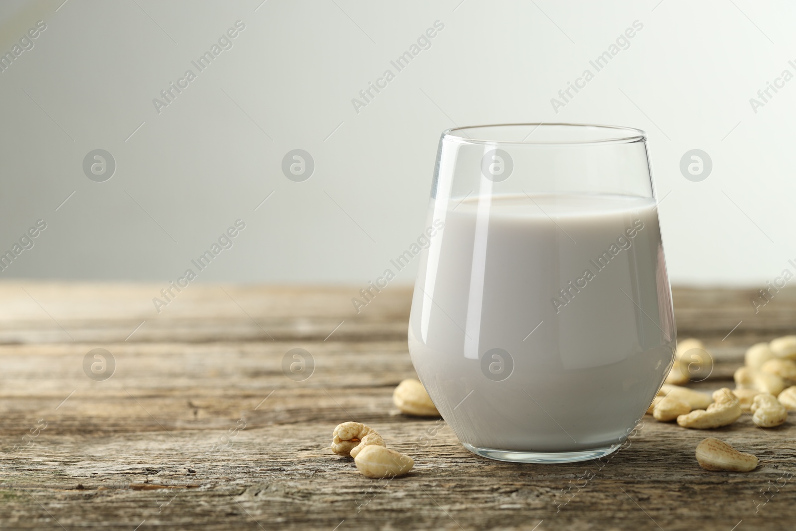 Photo of Fresh cashew milk in glass and nuts on wooden table against light background, closeup. Space for text