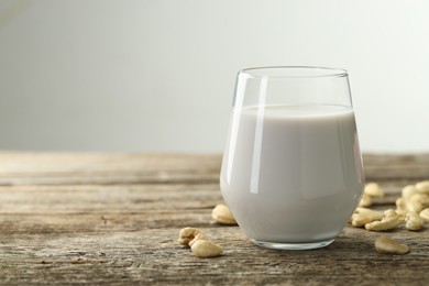 Photo of Fresh cashew milk in glass and nuts on wooden table against light background, closeup. Space for text