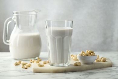 Photo of Fresh cashew milk in glass and nuts on white marble table against light background, closeup