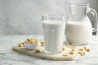 Photo of Fresh cashew milk in glass and nuts on white marble table against light background, closeup