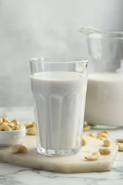 Photo of Fresh cashew milk in glass and nuts on white marble table against light background, closeup