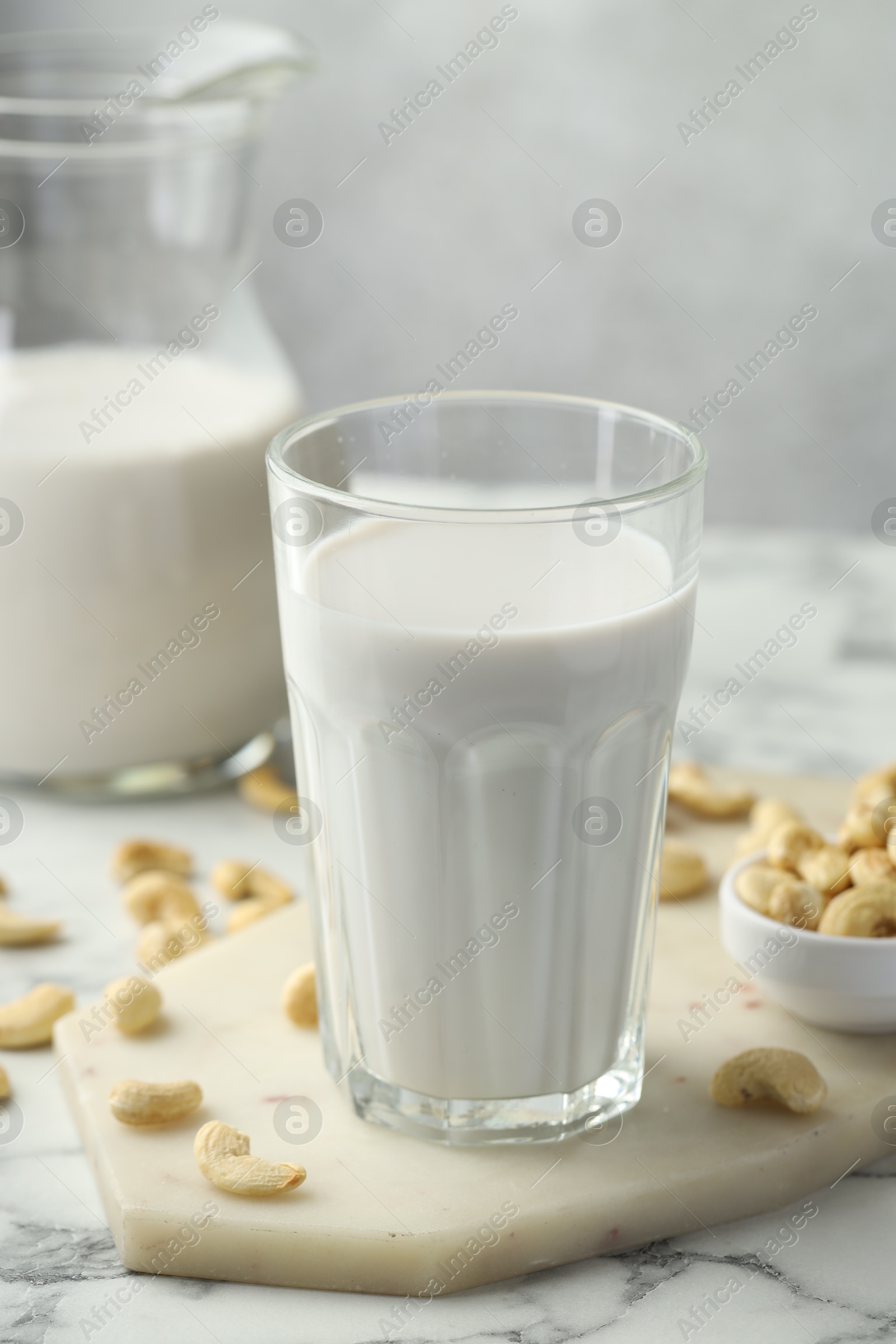 Photo of Fresh cashew milk in glass and nuts on white marble table against light background, closeup