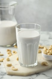 Photo of Fresh cashew milk in glass and nuts on white marble table against light background, closeup