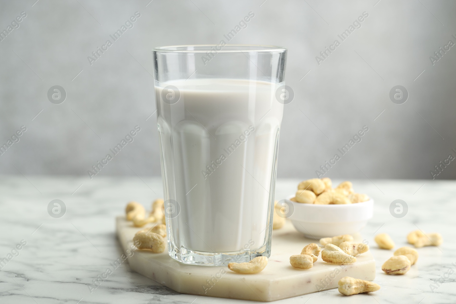 Photo of Fresh cashew milk in glass and nuts on white marble table against light background, closeup